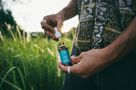 personne dans un champs au coucher du soleil ouvrant un flacon de Gouttes Mani au CBD et à la mélatonine