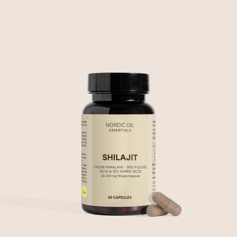 Bouteille en verre brun étiquetée Nordic Oil Essentials Shilajit avec deux capsules à côté sur fond beige.