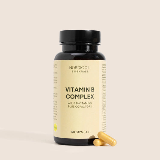 Bouteille noire de complément Vitamin B Complex de Nordic Oil Essentials avec deux capsules jaunes à côté sur fond beige.