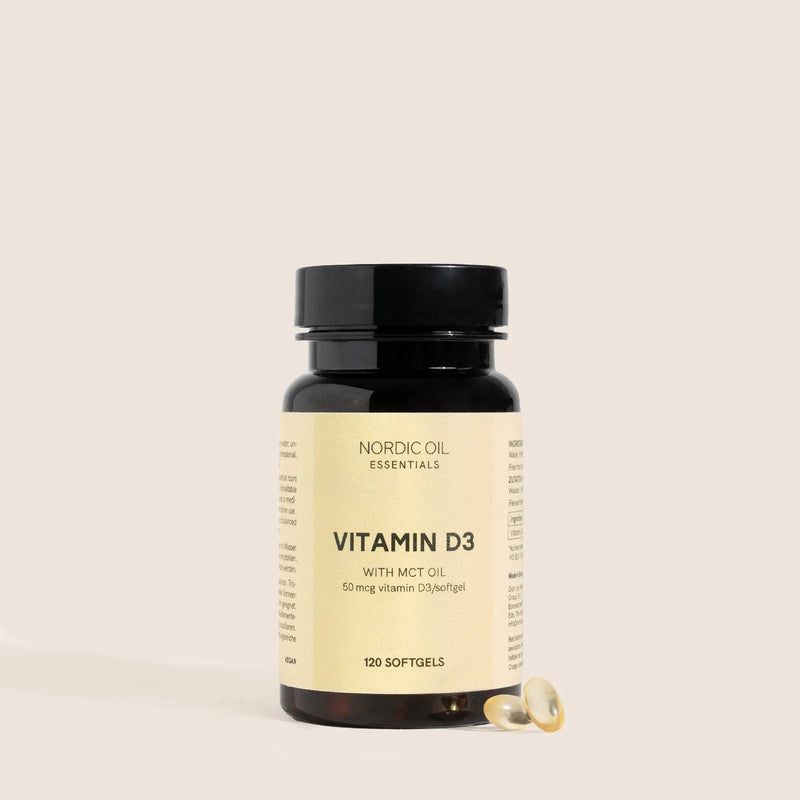 Flacon brun de vitamine D3 avec huile MCT et deux gélules à côté sur fond beige