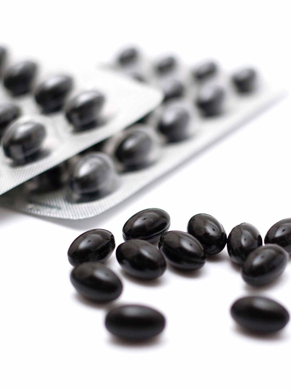 Gélules noires brillantes sur fond blanc près d'un blister