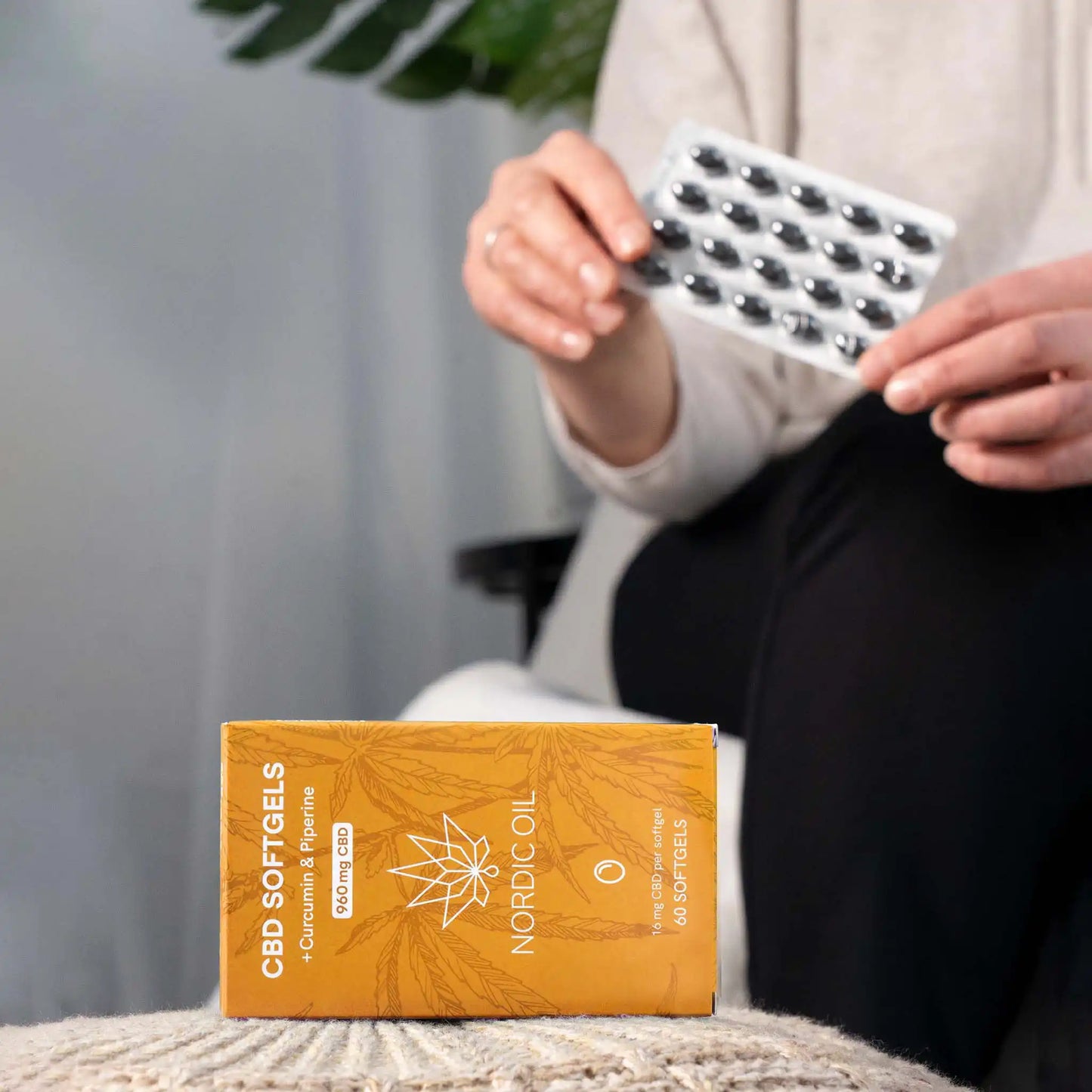 Au premier plan, l'emballage des capsules de CBD ; à l'arrière-plan, le client tient les capsules.