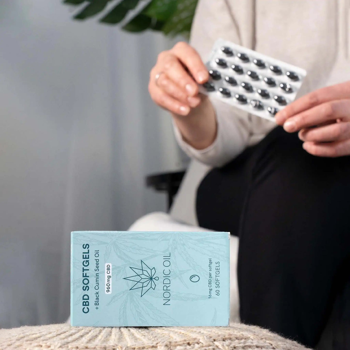 Au premier plan, l'emballage des capsules de CBD ; à l'arrière-plan, le client tient les capsules.
