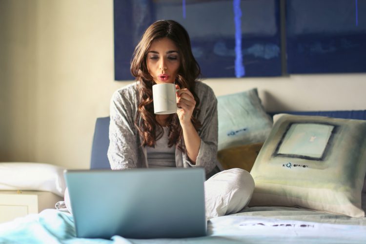 femme assise sur son lit avec ordinateur et café