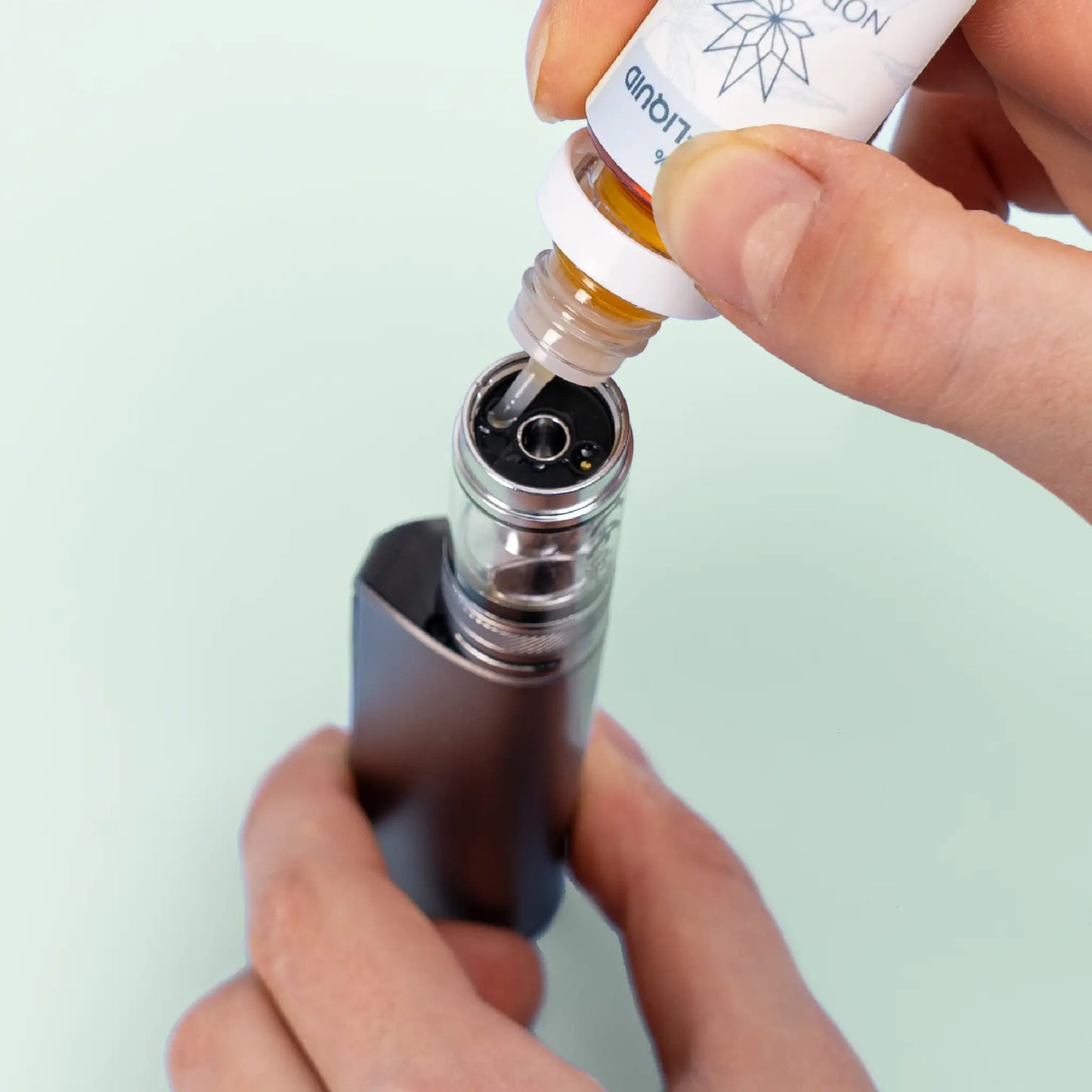 Une personne remplissant une e-cigarette avec Nordic Oil Myrtille E-Liquid 3%.
