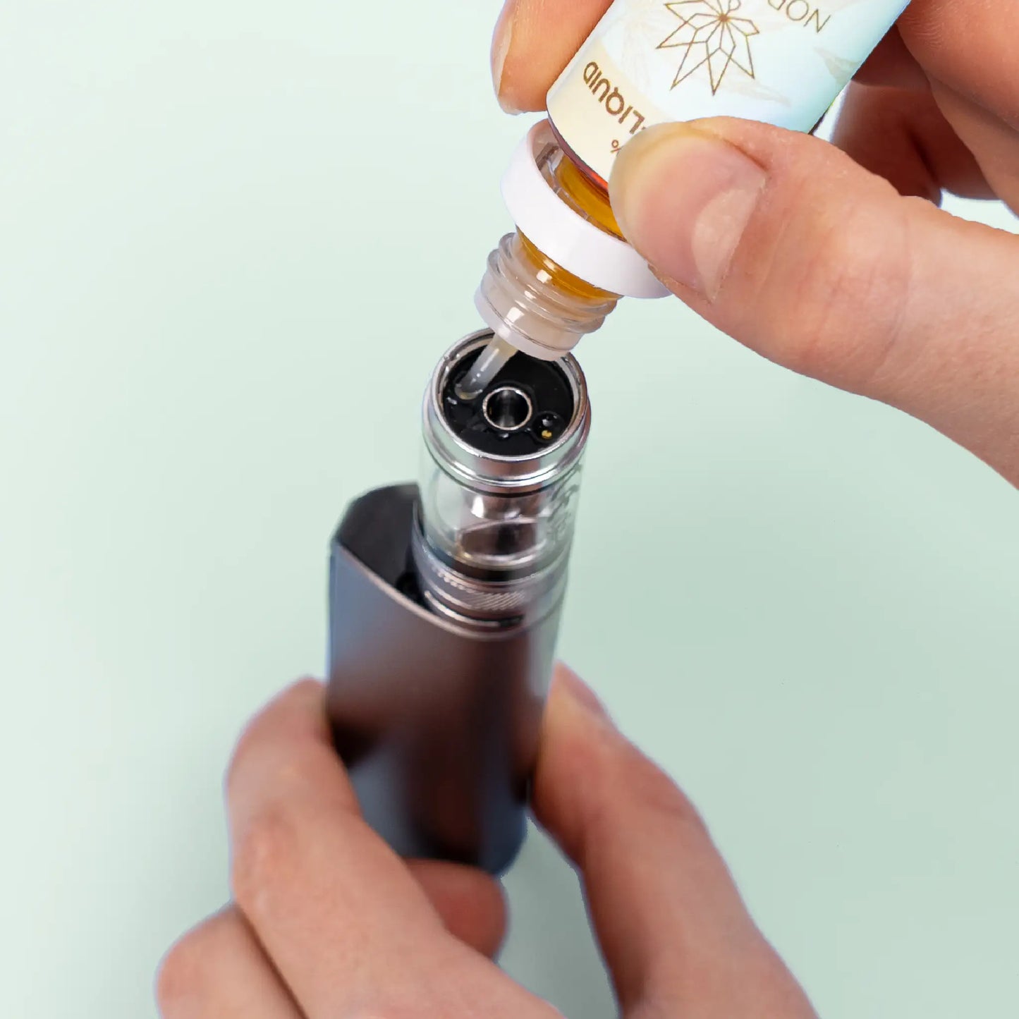Une personne remplissant une e-cigarette avec Nordic Oil Mangue E-Liquid 3%.
