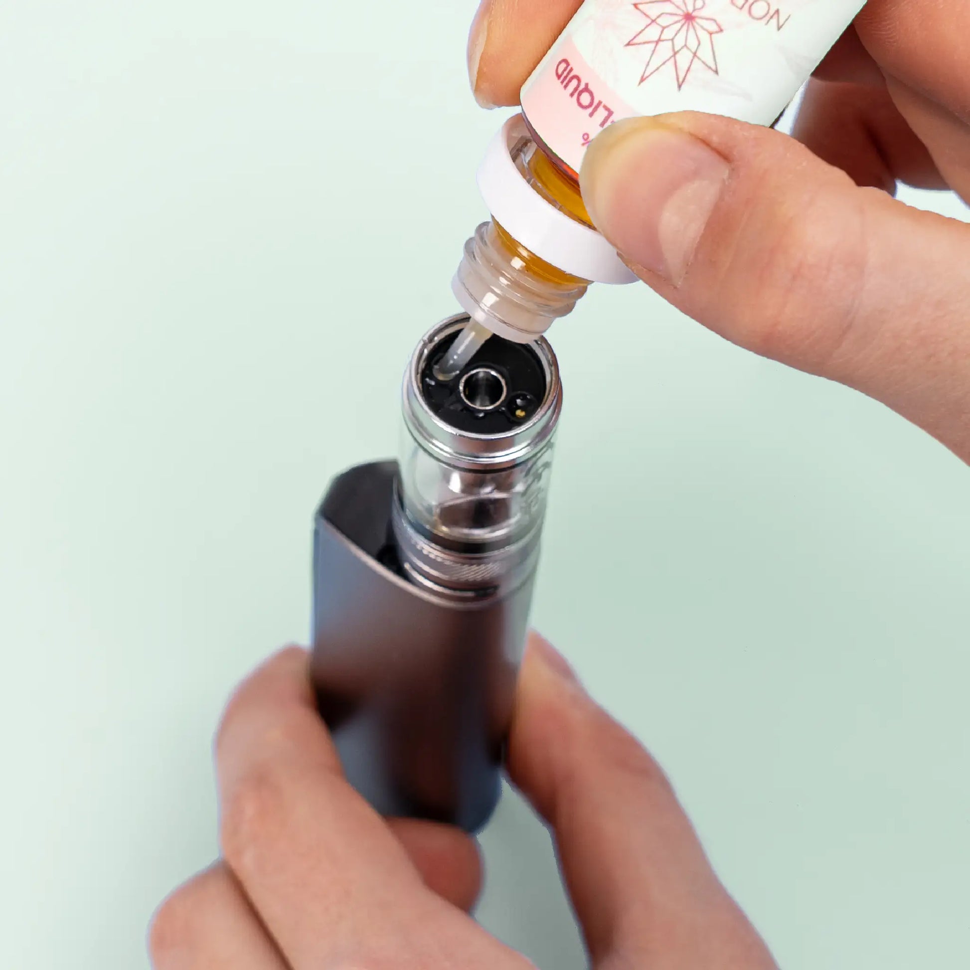 Une personne remplissant une e-cigarette avec Nordic Oil Pastèque & Menthe E-Liquid 3%.