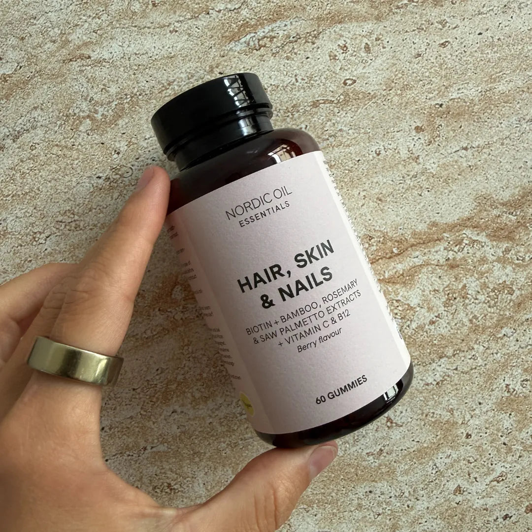 Gummies Nordic Oil Essentials Cheveux, Peau et Ongles – flacon brun tenu par une main, étiquette rose clair