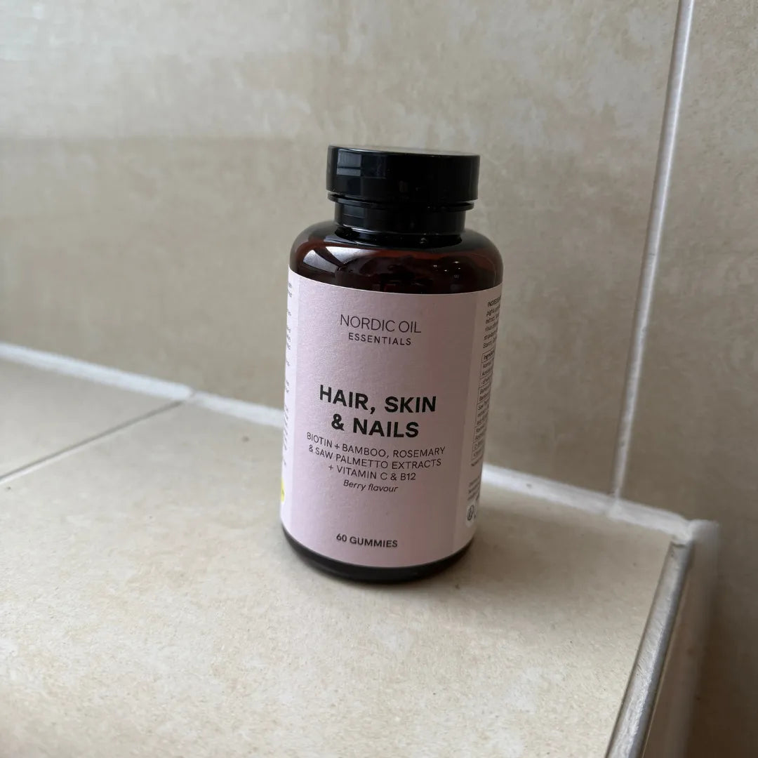 Flacon brun de gummies Nordic Oil Hair, Skin & Nails posé sur du carrelage