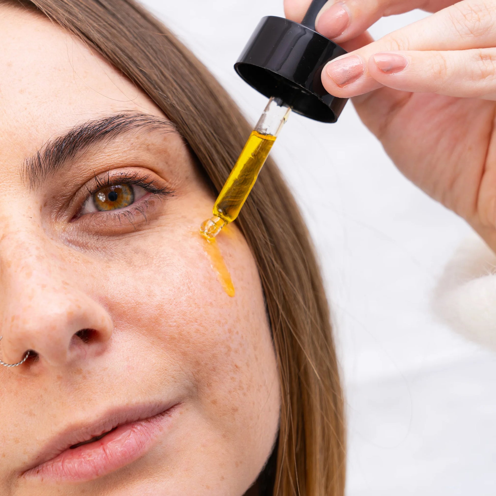 Une femme applique de l'huile CBD Nordic Oil sur son visage à l'aide d'un doseur.