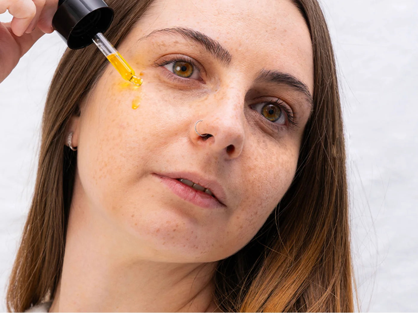 Une femme applique de l'huile CBD Nordic Oil sur son visage à l'aide d'un doseur.