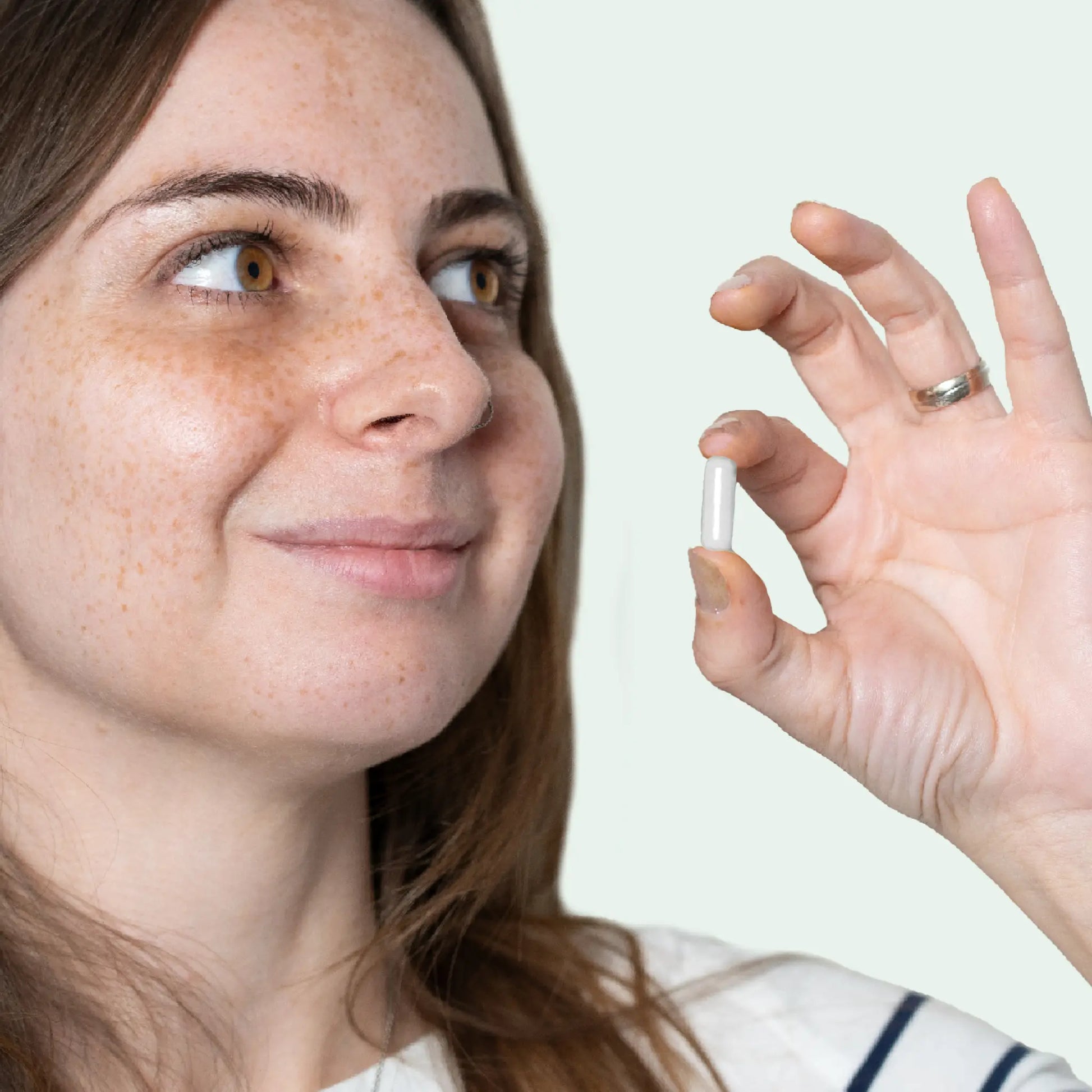 Femme souriante tenant une capsule blanche entre le pouce et l'index.